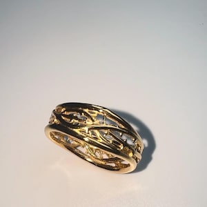 May include: A gold ring with a delicate, intricate design that resembles a woven branch pattern.