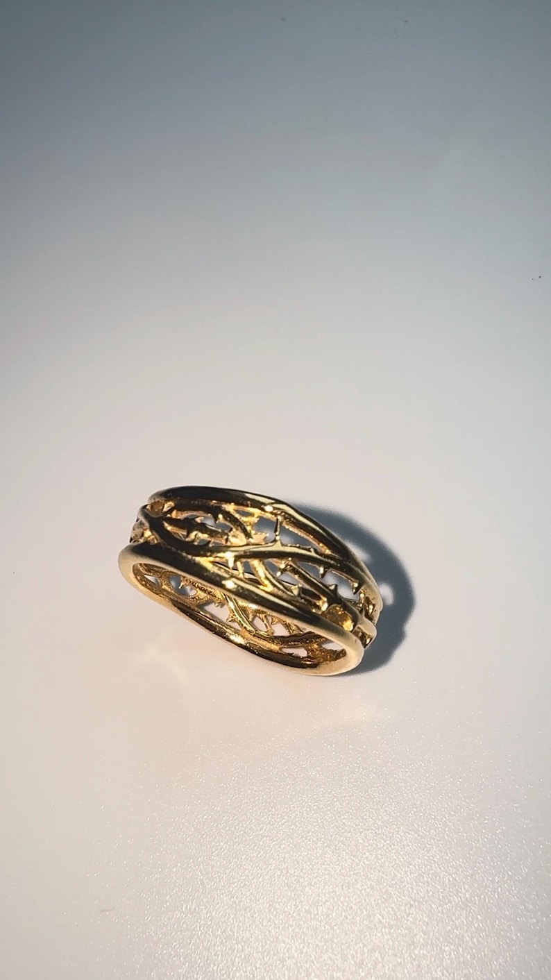 May include: A gold ring with a delicate, intricate design that resembles a woven branch pattern.