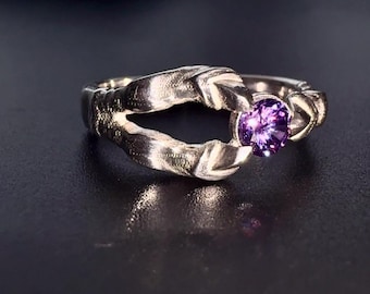 May include: A silver ring with a purple gemstone set in a unique, twisted design.