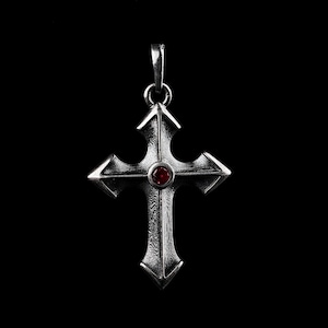 May include: A silver cross pendant with a red gemstone in the center. The cross has a detailed design with intricate edges.