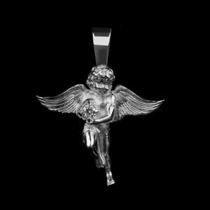 May include: Silver pendant featuring a detailed cherub with outstretched wings, holding a gem. The pendant has a polished finish and is suspended from a rectangular bail. The background is solid black, highlighting the pendant's design.