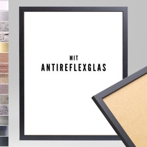 Op de afbeelding: Een zwarte fotolijst met een witte achtergrond en de tekst "MIT ANTIREFLEXGLAS" in zwart. De lijst is gemaakt van hout en heeft een eenvoudig ontwerp.