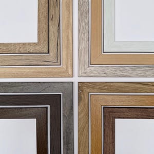 Può includere: Una collezione di cornici in legno in varie tonalità di marrone, grigio e beige. Le cornici hanno un design semplice e classico con forma quadrata o rettangolare. Gli angoli delle cornici sono smussati e le cornici sono disposte a griglia.