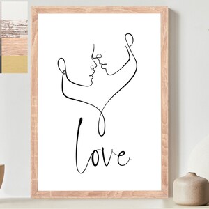 Op de afbeelding: Een zwart-witte lijntekening van twee mensen die kussen, met het woord "Love" eronder. De tekening is ingelijst in een licht houten lijst en hangt aan een witte muur.