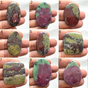 Puede incluir: Una colección de nueve piedras preciosas pulidas de varias formas, incluyendo ovaladas, rectangulares y en forma de lágrima. Las piedras muestran una mezcla de colores, como rojo intenso, verde y marrón, con patrones y texturas únicos. Cada piedra se sostiene en una mano.