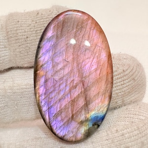 May include: A large, oval-shaped, polished labradorite gemstone with a pink, purple, and blue iridescent sheen.