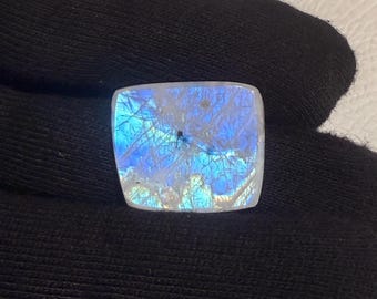 May include: A square-shaped, iridescent gemstone with a blue and white color scheme. The gemstone has a smooth, polished surface and a translucent appearance.