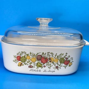 May include: White casserole dish with a clear glass lid. The dish features a colorful vegetable design with tomatoes, lemons, and other produce. The text "L'échalote La Sauge" is printed on the front.