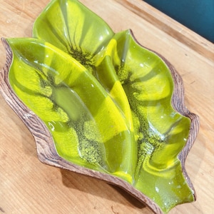 May include: A ceramic divided serving dish shaped like a large leaf with three distinct sections. The interior features a vibrant lime green and yellow glaze with dark green speckled accents, while the outer edge has a textured brown wood-grain finish.
