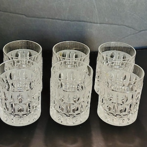 May include: A set of six clear glass tumblers arranged in two rows of three. Each cylindrical glass features a repeating geometric pattern of vertical etched lines and diamond shapes around the exterior surface, with a smooth, thick base.