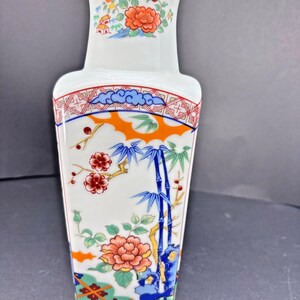 May include: White ceramic vase with a rectangular body and flared top. The vase features colorful floral and bamboo designs in orange, blue, and green. The design includes a red and blue border.