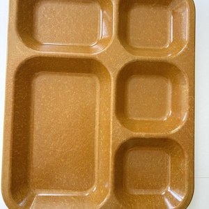 May include: A rectangular mustard-yellow cafeteria tray featuring a large main compartment on the left and four smaller, square-shaped compartments on the right. The tray has a textured, speckled finish throughout its entire surface.