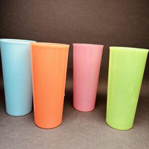 May include: A set of four tall, cylindrical drinking tumblers in solid pastel colors. The collection includes one light blue, one orange, one pink, and one lime green cup, each featuring a smooth, opaque finish and a simple, straight-sided design.