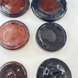 May include: A collection of six circular, flat objects arranged in two columns. The left column features three reddish-brown discs with varying surface details, while the right column displays three black discs, including one with a cross-shaped indentation.