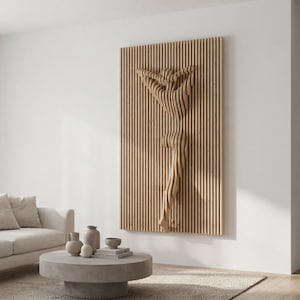 Könnte beinhalten: Ein Wandkunstwerk aus Holz mit einer stilisierten menschlichen Figur. Die Figur besteht aus geschichteten Holzlatten, die einen dreidimensionalen Effekt erzeugen. Das Kunstwerk ist auf einer vertikalen Platte mit vertikalen Holzlatten montiert. In einem modernen Wohnzimmer.
