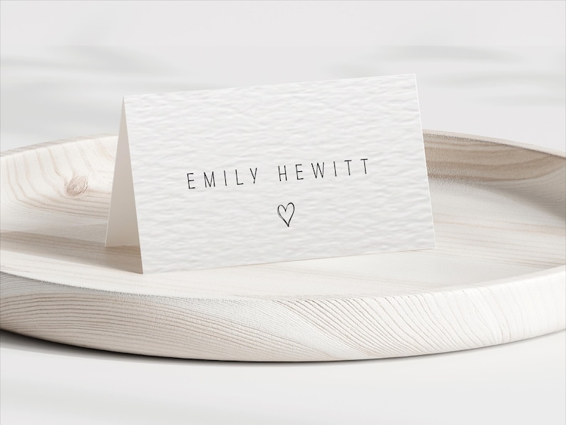 Pu&ograve; includere: Un biglietto bianco piegato con il nome "EMILY HEWITT" stampato in nero, con un piccolo simbolo a forma di cuore sotto. Il biglietto &egrave; su un vassoio di legno chiaro, adatto per matrimoni o eventi speciali.