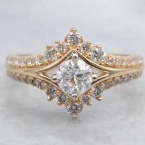 Pode incluir: Um anel de noivado de ouro com uma grande pedra central de diamante clara e redonda. O anel apresenta um halo de diamantes menores e uma banda cravejada de diamantes. A cravação é um design delicado e intrincado.