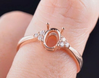 Puede incluir: Engaste de anillo de oro rosa con engaste de garras para una piedra preciosa de forma ovalada. El anillo tiene pequeños diamantes a cada lado del engaste.