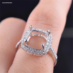 May include: A silver ring with a square-shaped setting surrounded by small diamonds. The ring is designed to hold a larger gemstone in the center.
