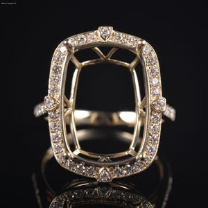 May include: A gold ring setting featuring a large, rectangular, open-center basket design. The frame is adorned with small, round, clear stones set along the perimeter and the band. The structure includes four prominent prongs at the corners.