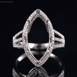 May include: A silver ring with a marquise-shaped setting surrounded by small diamonds. The ring has three bands with small diamonds set in them.