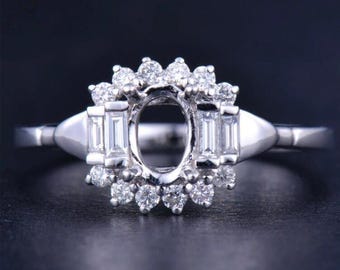 Puede incluir: Un engaste de anillo de plata con una gran piedra central ovalada y un halo de diamantes redondos más pequeños. El anillo tiene una banda delicada y está engastado con diamantes baguette a cada lado de la piedra central.