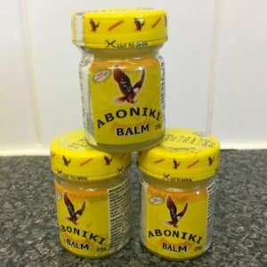 Op de afbeelding: Drie gele potjes AboniKi balsem, elk met een rood adelaarlogo en de tekst "AboniKi Balm 25g" op het etiket.
