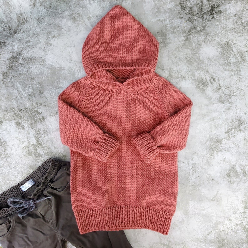 May include: A coral pink knitted hooded sweater with long sleeves and a ribbed hem.