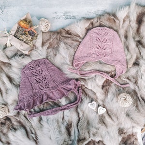 May include: Two pink crocheted baby hats with delicate lace patterns. The hats are displayed on a faux fur background with decorative hearts.