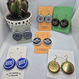 Puede incluir: Pendientes hechos a mano con tapas de botellas de cerveza, que muestran varias marcas de cerveza como Heineken, Leffe, Corona Extra y Super Bock. Cada par se presenta en una tarjeta con un logotipo de corazón. Accesorio único.