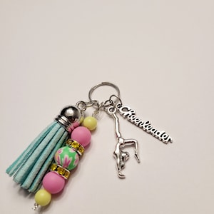 May include: A light blue tassel keychain with pink, yellow and green beads. The keychain also features a silver charm of a cheerleader doing a back handspring and a silver charm with the word "Cheerleader".