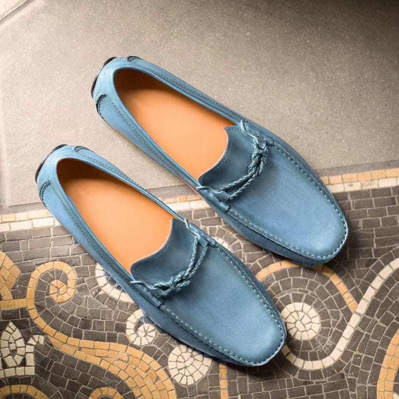 May include: A pair of light blue leather loafers with a braided leather detail on the front. The loafers are on a patterned tile floor.