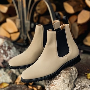 May include: A pair of beige suede Chelsea boots with black elastic side panels. The boots have a rounded toe and a chunky heel.
