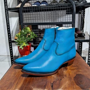 May include: A pair of blue leather ankle boots with a pointed toe and a zip on the side. The boots have a distressed look and are made from soft, supple leather.