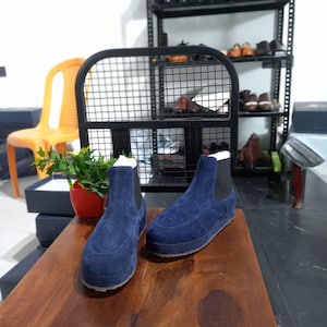 May include: Two pairs of blue suede ankle boots with black soles and elastic sides. The boots are sitting on a wooden table.