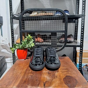 Könnte beinhalten: Ein Paar schwarze Leder-Sneaker mit niedrigem Schaft und einem Kroko-Prägemuster. Die Schuhe haben schwarze Schnürsenkel und eine weiße Gummisohle.