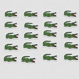 Può includere: Una collezione di ventinove toppe ricamate individuali, ognuna raffigurante un coccodrillo verde con bocca rossa e denti bianchi, disposte in uno schema a griglia su uno sfondo chiaro e uniforme per una presentazione ordinata.