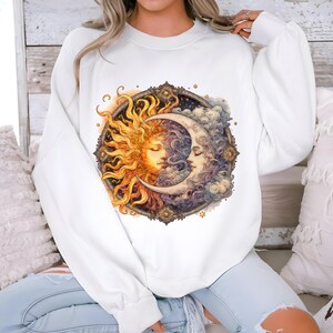May include: White sweatshirt with a graphic print of a sun and moon with faces. The sun is yellow and orange, and the moon is white and blue. The graphic is surrounded by a decorative frame.