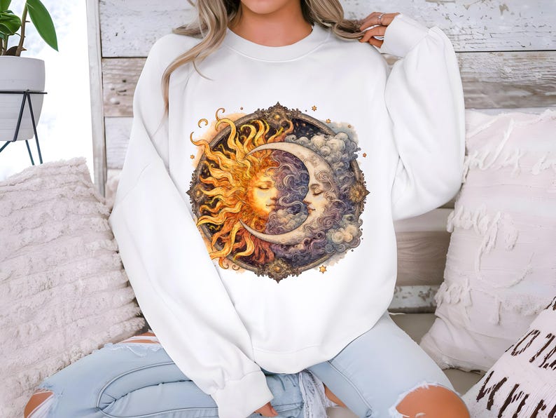 May include: White sweatshirt with a graphic print of a sun and moon with faces. The sun is yellow and orange, and the moon is white and blue. The graphic is surrounded by a decorative frame.