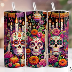 Op de afbeelding: Drie roestvrijstalen bekers met rietjes, met een levendig ontwerp voor de Dag van de Doden. Elke beker toont een kleurrijke suikerschedel omringd door bloemen, kaarsen en feestelijke versieringen tegen een zwarte achtergrond. Het ontwerp bevat het woord "Seamless".