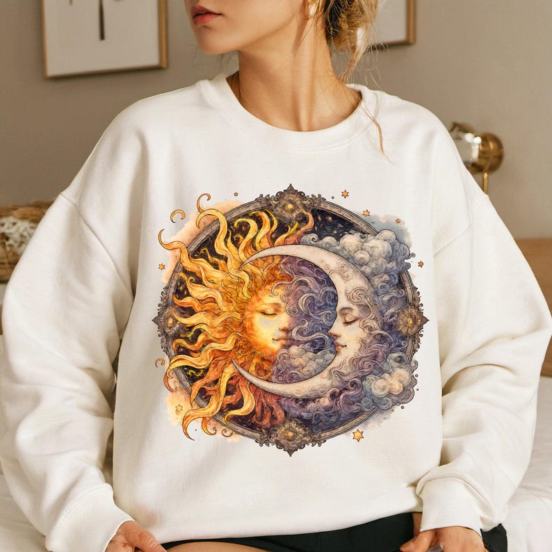 May include: White sweatshirt with a graphic print of a sun and moon with faces. The sun is yellow and orange, and the moon is purple and blue. The graphic is surrounded by a decorative frame with stars.