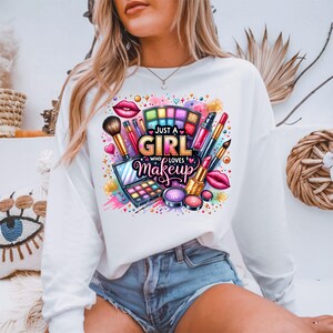 May include: White long-sleeve sweatshirt with a colorful graphic design of makeup products and the text "Just a Girl Who Loves Makeup".