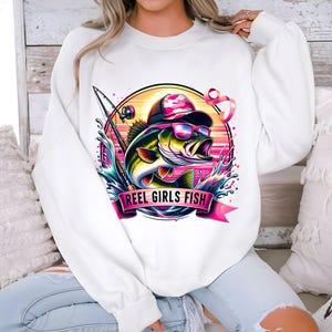 May include: White sweatshirt with a pink ribbon, a fishing rod, and a bass fish with a hat and sunglasses. The text "Reel Girls Fish" is printed on the sweatshirt.