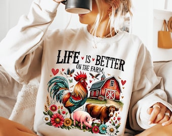 May include: White sweatshirt with a graphic design of a rooster, a pig, a cow, a red barn, and flowers. The text on the sweatshirt reads "Life is better on the farm."