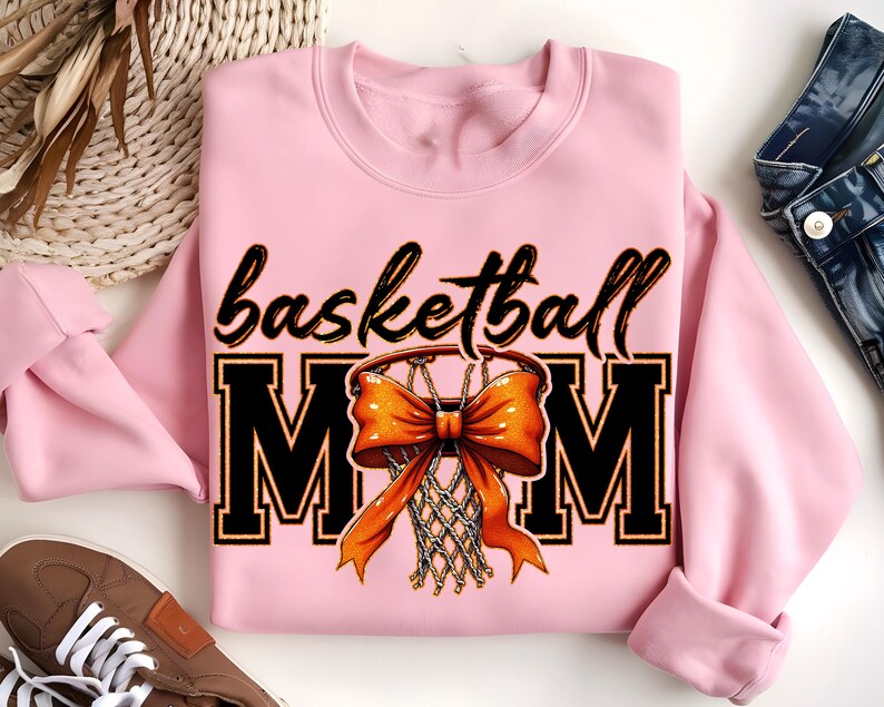 May include: Pink sweatshirt with the text "basketball mom" in black letters and a basketball hoop with an orange bow on it.