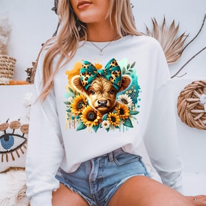 May include: White sweatshirt with a graphic of a brown and white calf wearing a teal and leopard print bow. The calf is surrounded by yellow sunflowers and white flowers.