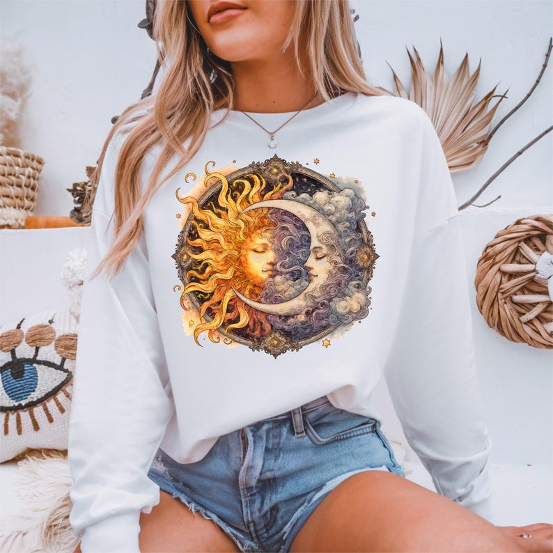 May include: White long-sleeve sweatshirt with a graphic print of a sun and moon with faces, surrounded by stars and clouds.