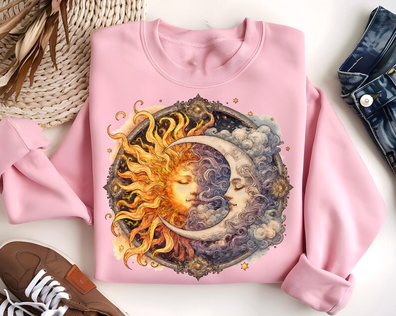 May include: Pink sweatshirt with a graphic print of a sun and moon with a celestial design. The sun and moon are depicted as faces with closed eyes.