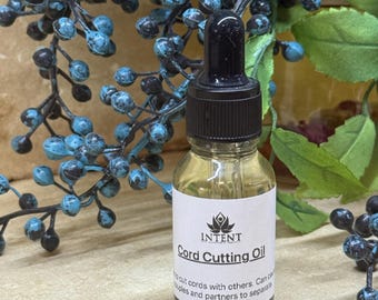 May include: A small glass bottle of "Cord Cutting Oil" with a black dropper top. The label reads "INTENT" and describes the oil's purpose. The bottle is set against a backdrop of blue berries and green leaves.