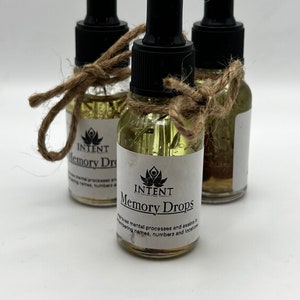 May include: Three small glass bottles with dropper tops, tied together with twine. Each bottle contains a clear liquid and has a white label with black text that reads "INTENT Memory Drops" and describes the product as improving mental processes and assisting in remembering names, numbers, and locations.